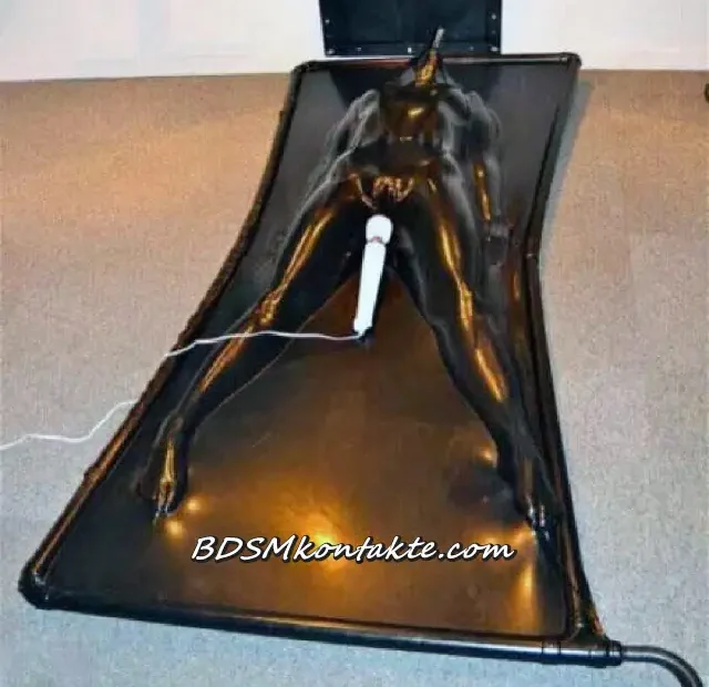 Person in schwarzem Latex-Vakuumbett auf dem Boden mit weißem Vibrator